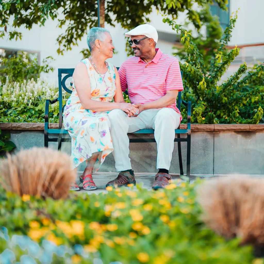 A senior couple sit, hand-in-hand on a metal bench in a park