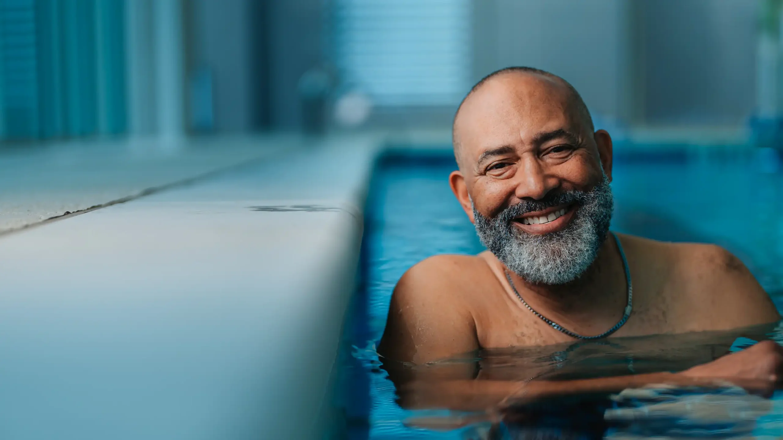 A senior man stands to the wall while in an indoor swimming pool