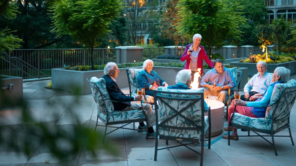 A group of senior adults spend time talking around an outdoor fireplace