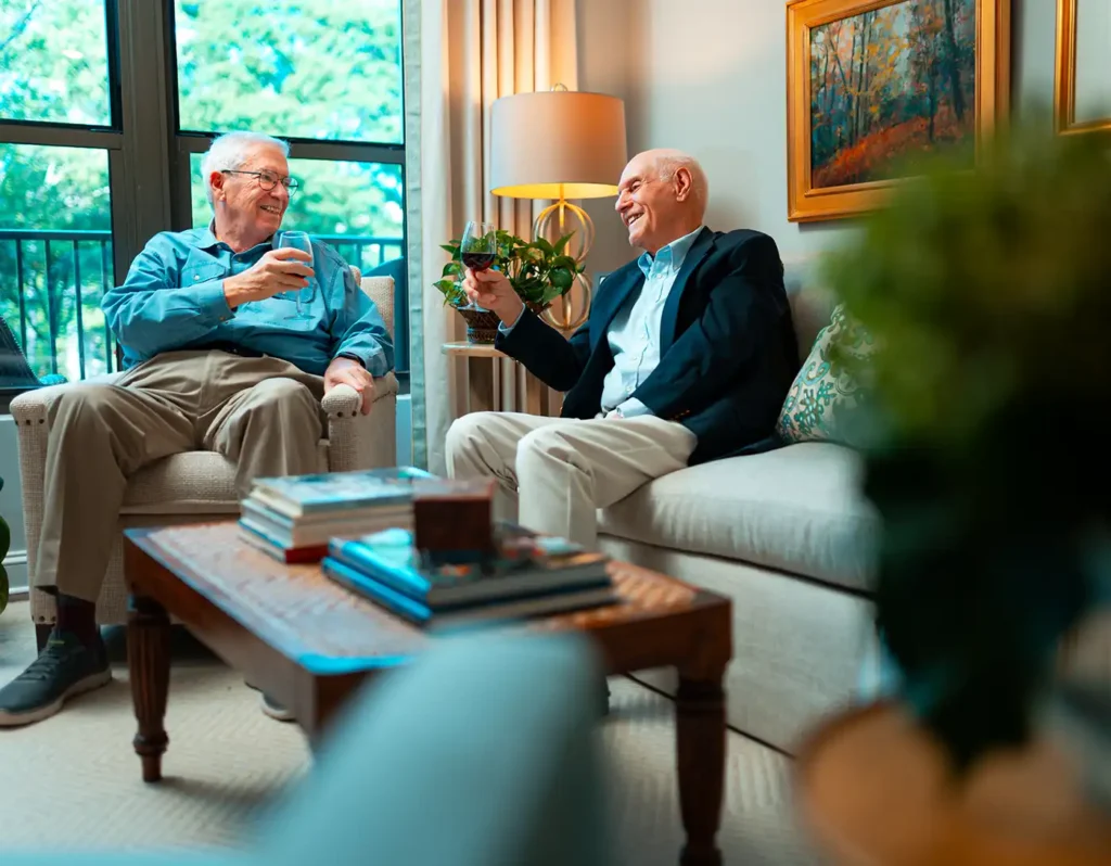 Two senior men toast a glass of wine in a living room