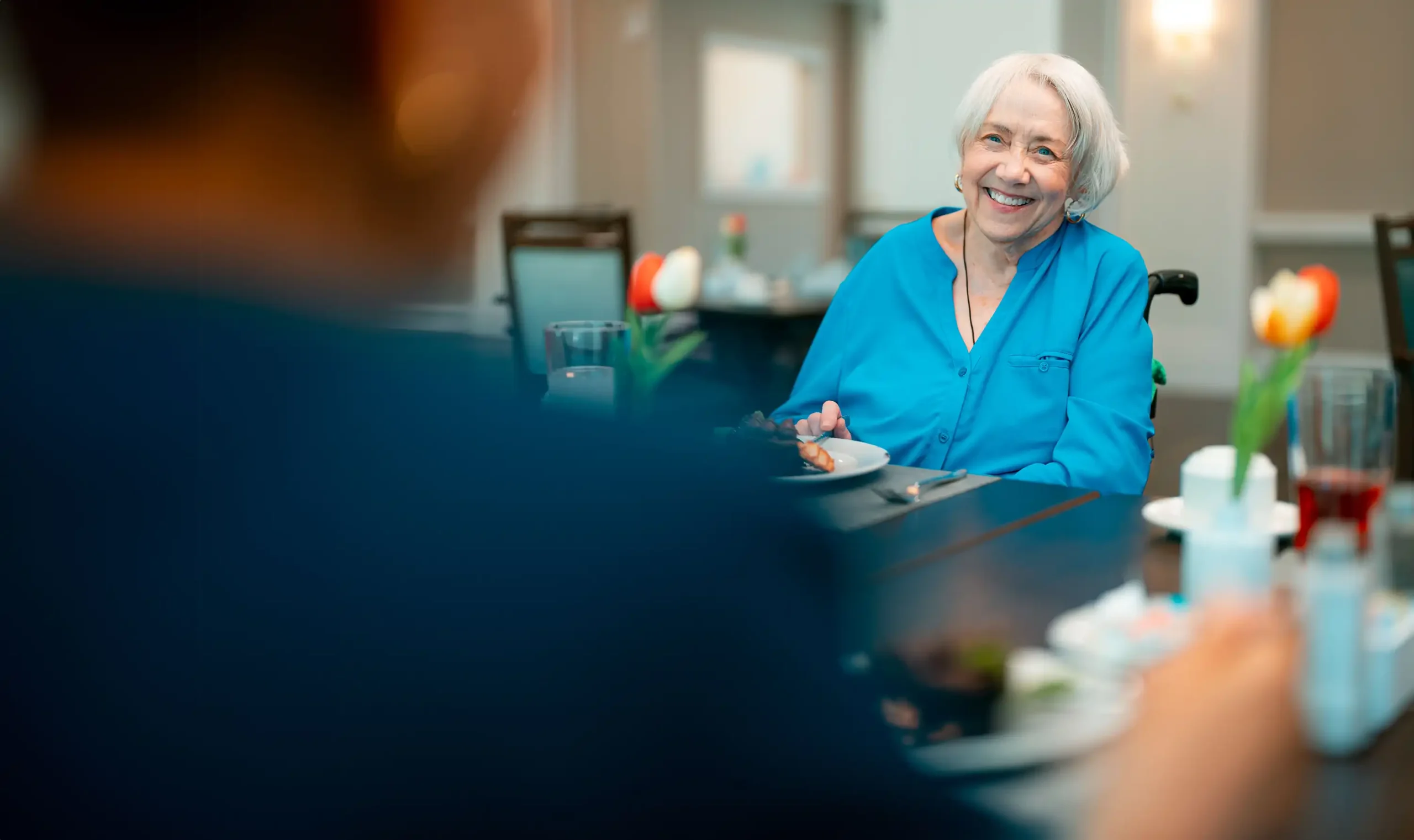 A senior woman sits across from a friend in a restaurant setting