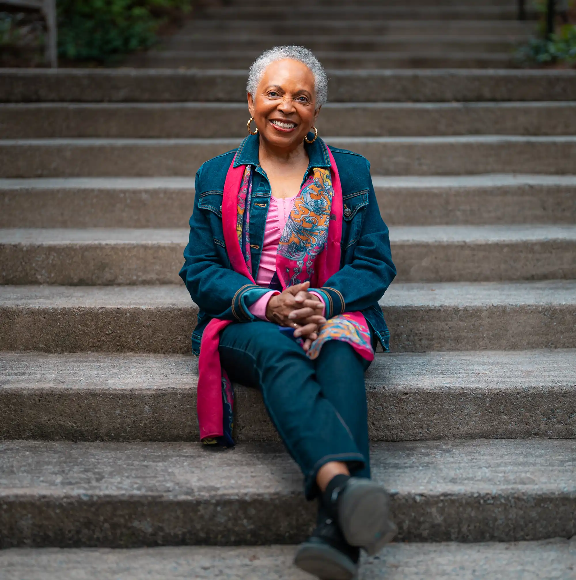 A senior woman sits on a concrete staircase with her ankles crossed