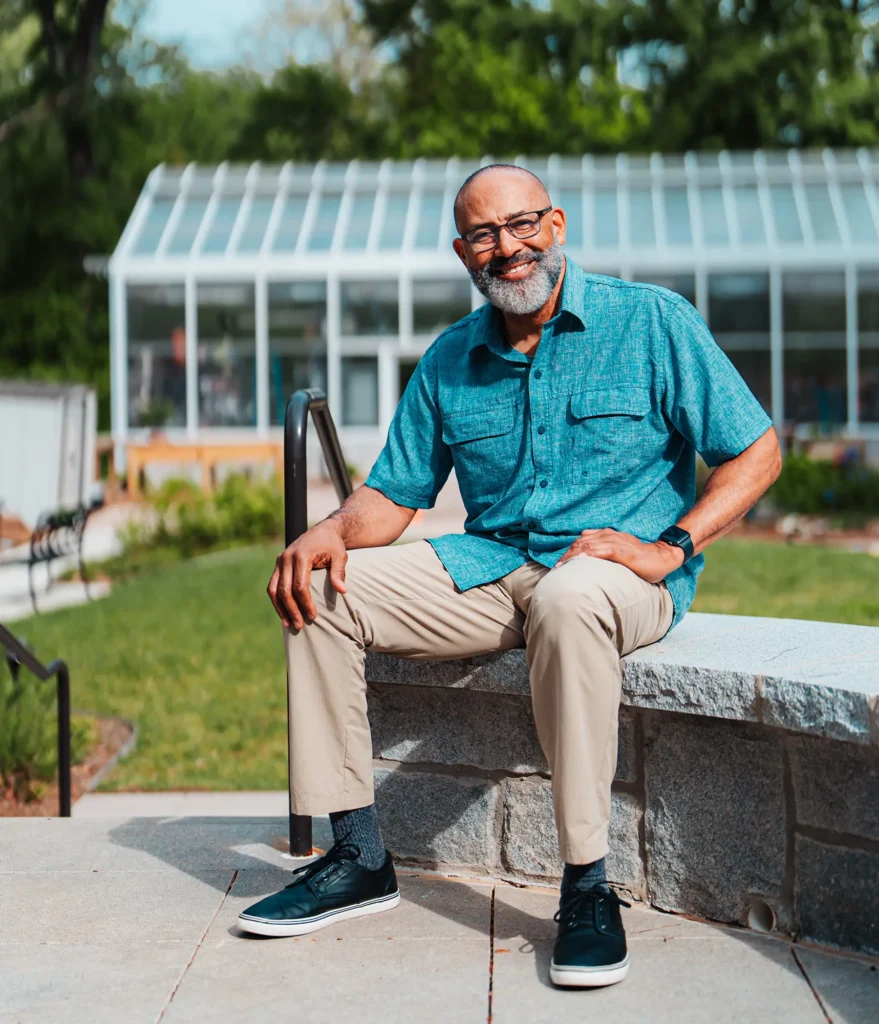 A senior man sits in front of the greenhouse at Canterbury Court